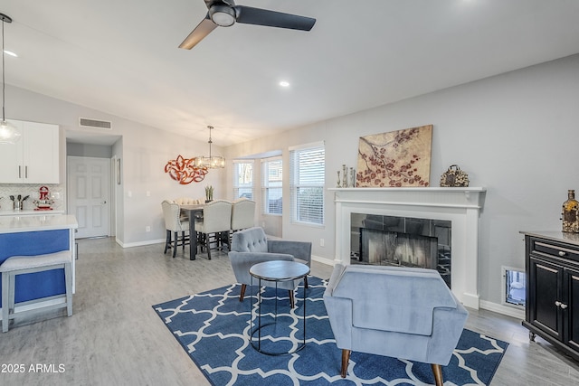 living room featuring a tiled fireplace, vaulted ceiling, ceiling fan with notable chandelier, and light wood-type flooring