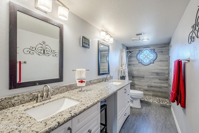 bathroom with hardwood / wood-style floors, vanity, walk in shower, toilet, and a textured ceiling