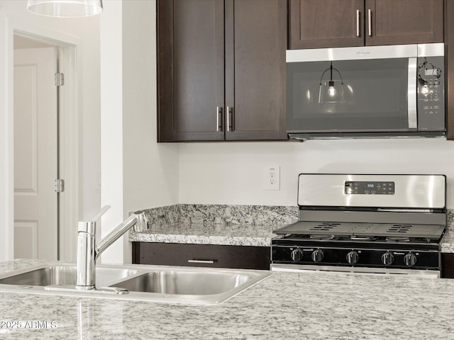 kitchen featuring stainless steel appliances, light stone countertops, sink, and dark brown cabinetry