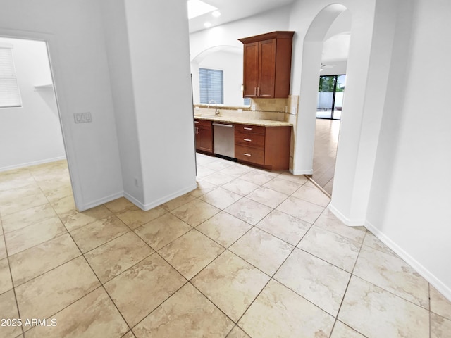 hall with arched walkways, light tile patterned floors, a sink, and baseboards