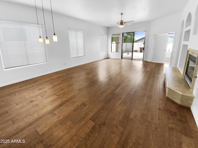 unfurnished living room featuring a ceiling fan, a tile fireplace, dark wood-style floors, and baseboards