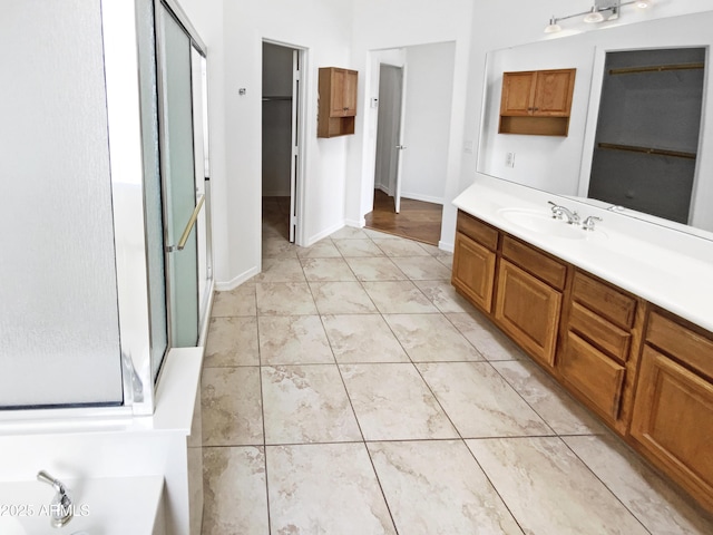 bathroom with a spacious closet, a shower stall, vanity, a bath, and baseboards