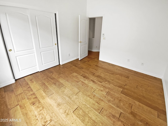 unfurnished bedroom featuring light wood-style floors, baseboards, and a closet