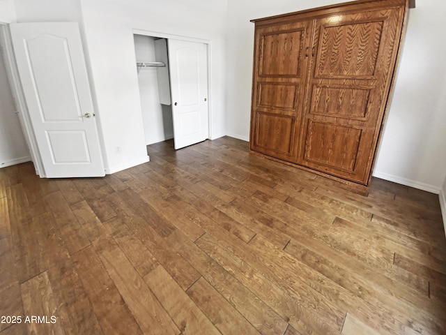 unfurnished bedroom featuring dark wood-style flooring, a closet, and baseboards