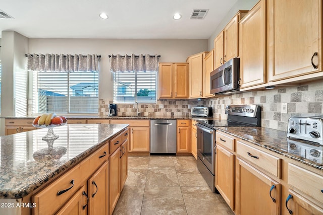 kitchen featuring stainless steel appliances, sink, backsplash, and dark stone counters