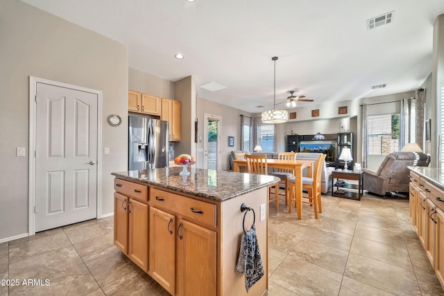 kitchen with light tile patterned floors, ceiling fan, a center island, stainless steel refrigerator with ice dispenser, and dark stone counters