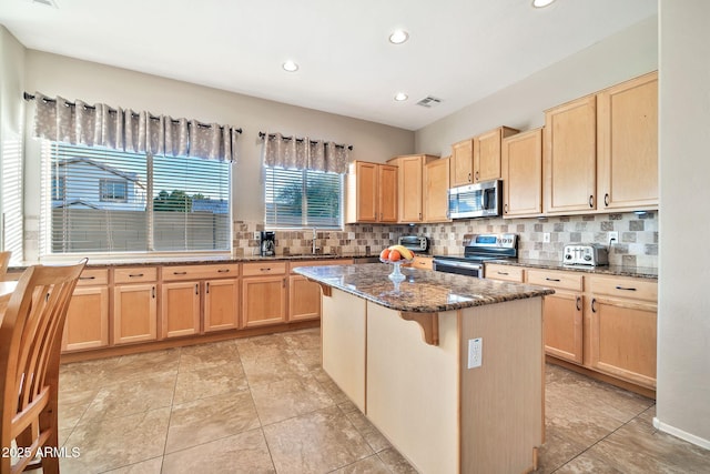 kitchen with sink, a breakfast bar, dark stone countertops, stainless steel appliances, and a center island