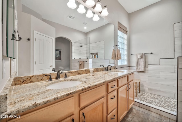 bathroom with a tile shower, vanity, and tile patterned flooring