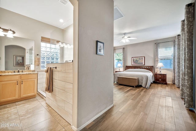 bedroom featuring ceiling fan, connected bathroom, light hardwood / wood-style floors, and sink