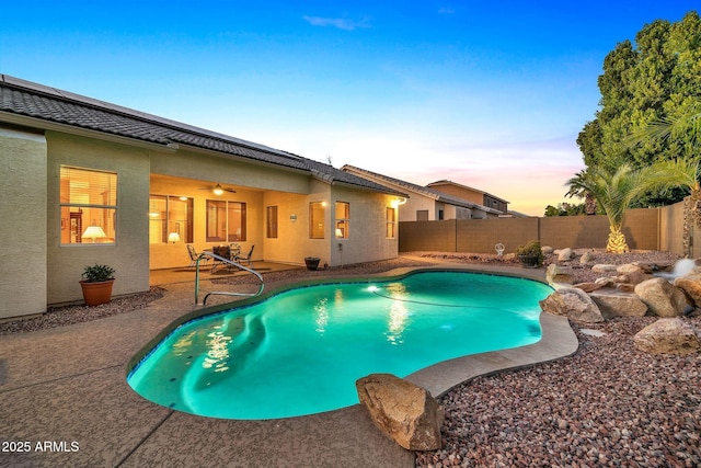 pool at dusk featuring ceiling fan and a patio area