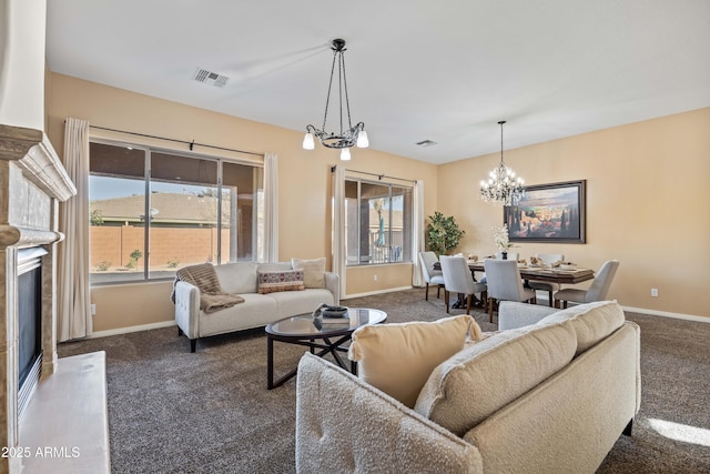 living area with visible vents, baseboards, dark colored carpet, a glass covered fireplace, and an inviting chandelier