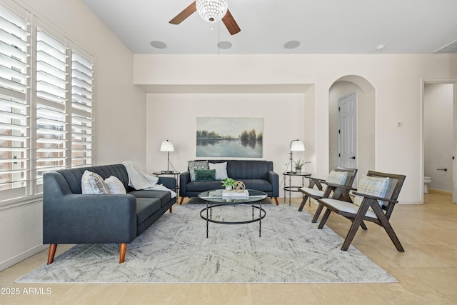 living room featuring arched walkways, ceiling fan, light tile patterned floors, and baseboards