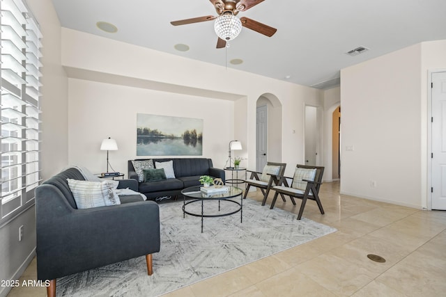 living area with arched walkways, light tile patterned floors, visible vents, a ceiling fan, and baseboards