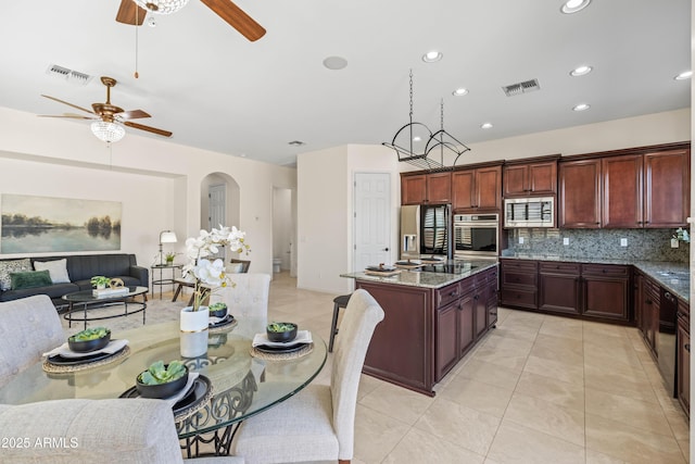 kitchen with visible vents, light stone counters, open floor plan, a kitchen island with sink, and stainless steel appliances