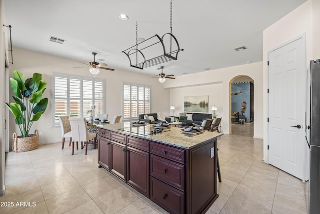 kitchen with arched walkways, light stone countertops, visible vents, and a center island