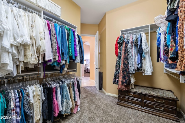 walk in closet featuring arched walkways and light colored carpet