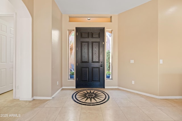 foyer entrance with arched walkways, baseboards, and light tile patterned floors