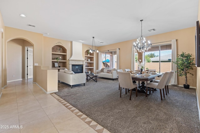 dining room with built in shelves, light tile patterned flooring, a fireplace, visible vents, and an inviting chandelier