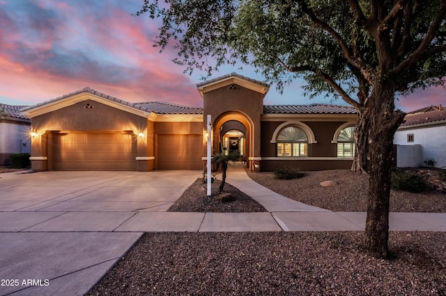 mediterranean / spanish-style house with a garage, concrete driveway, a tiled roof, and stucco siding