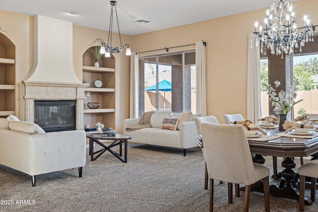 dining room with a large fireplace, visible vents, built in features, carpet, and a notable chandelier