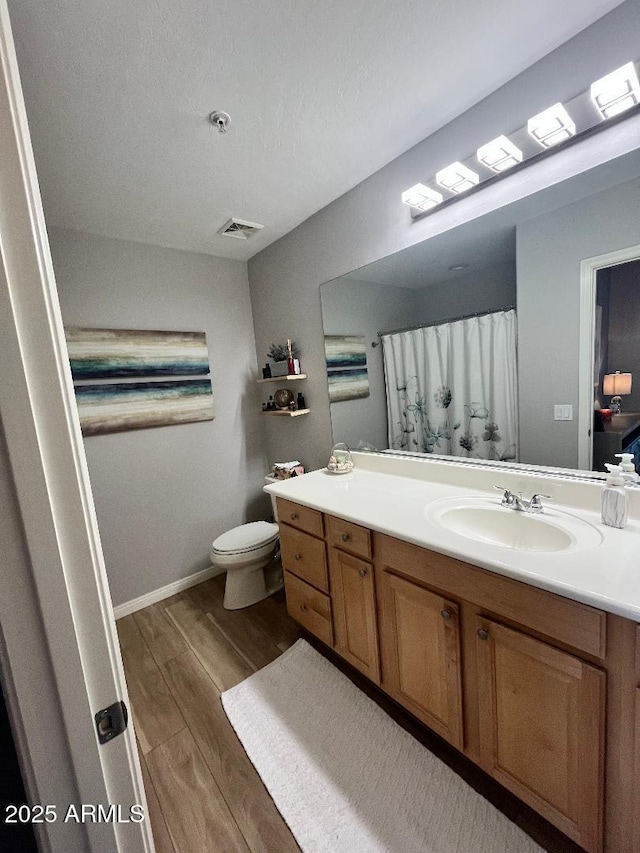 bathroom featuring visible vents, vanity, wood finished floors, toilet, and baseboards