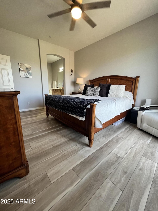 bedroom featuring ensuite bath, arched walkways, a ceiling fan, baseboards, and wood finished floors