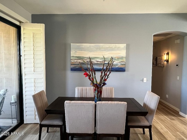 dining space featuring arched walkways, baseboards, and wood finished floors