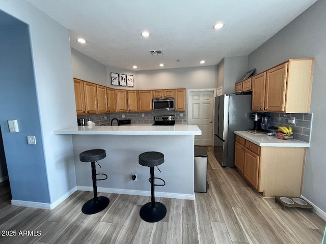 kitchen with visible vents, a kitchen bar, light wood-type flooring, tasteful backsplash, and stainless steel appliances