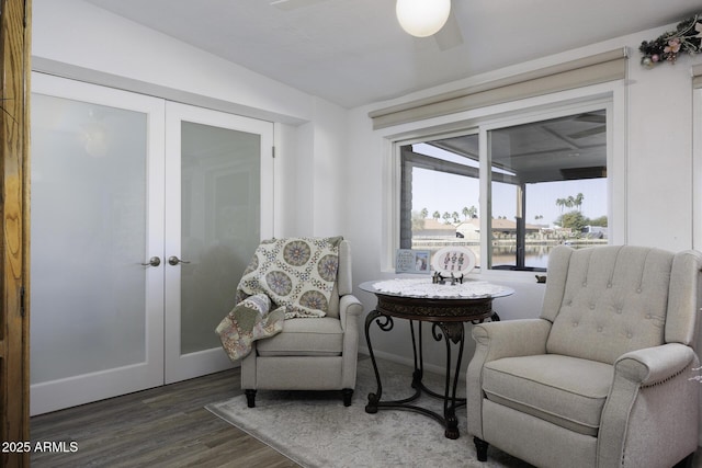 sitting room with french doors, dark hardwood / wood-style floors, ceiling fan, and a water view