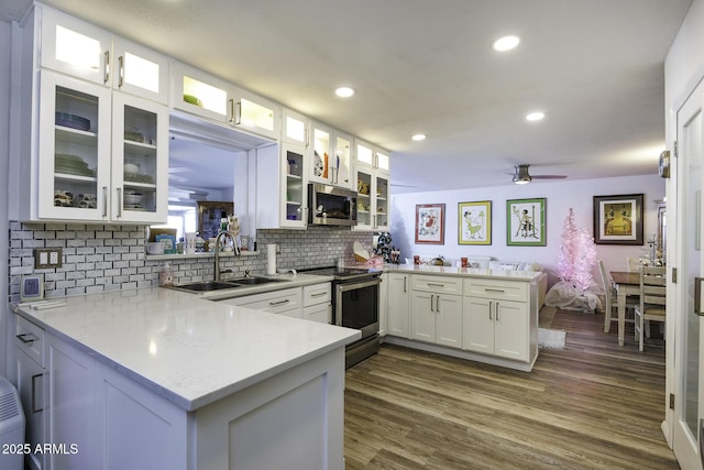 kitchen with sink, kitchen peninsula, decorative backsplash, white cabinets, and appliances with stainless steel finishes