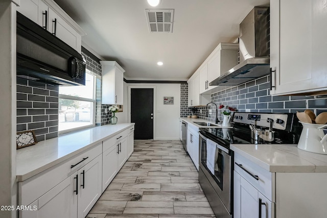 kitchen with appliances with stainless steel finishes, white cabinetry, sink, decorative backsplash, and wall chimney range hood