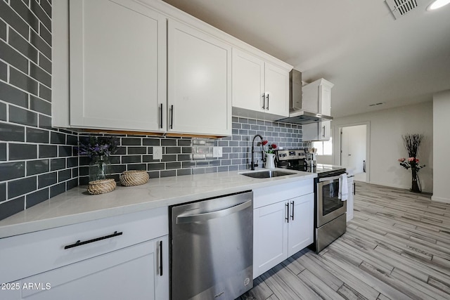 kitchen featuring appliances with stainless steel finishes, sink, wall chimney range hood, and white cabinets