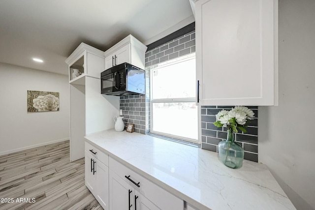 kitchen with light stone counters, light hardwood / wood-style floors, decorative backsplash, and white cabinets