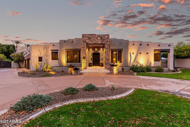 adobe home featuring stone siding, curved driveway, a yard, and stucco siding