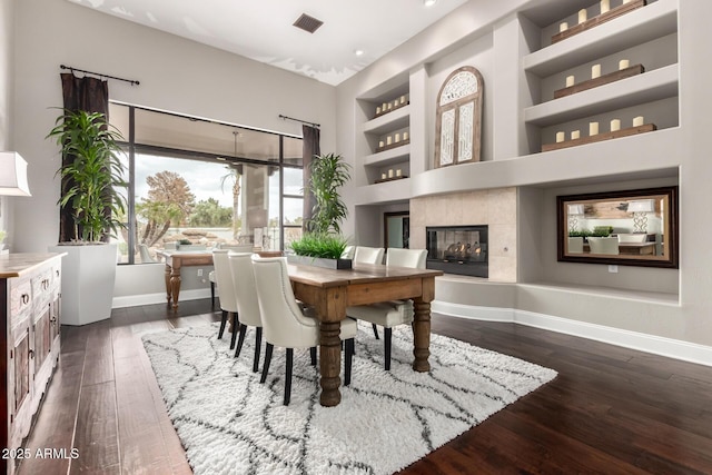 dining area with built in features, baseboards, visible vents, a tile fireplace, and dark wood-type flooring