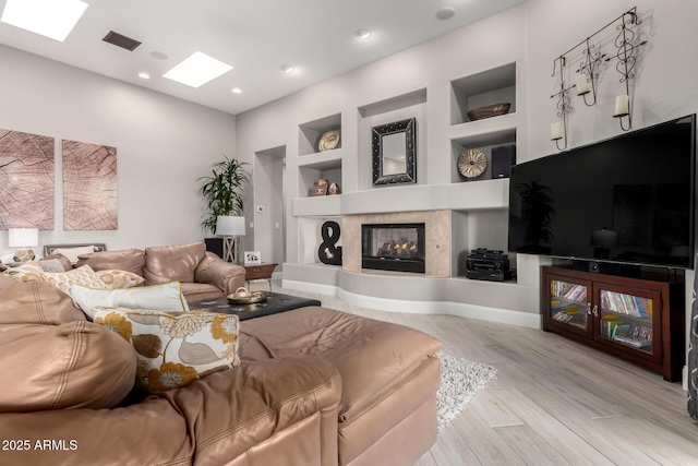 living area with visible vents, built in features, wood finished floors, a skylight, and a multi sided fireplace