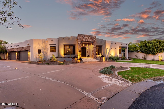 adobe home with a garage, stone siding, curved driveway, and a front yard