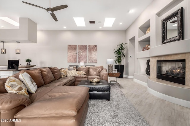 living area with built in features, a ceiling fan, visible vents, a skylight, and light wood-style flooring