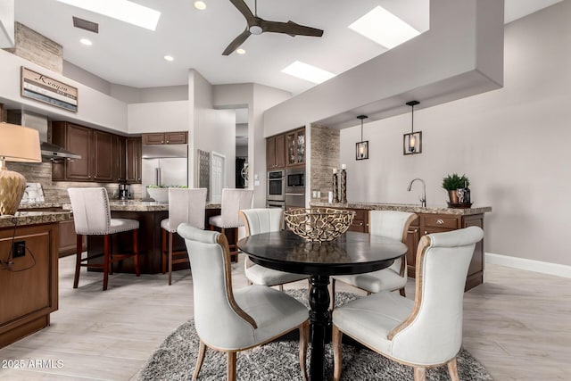 dining space with a ceiling fan, visible vents, baseboards, a skylight, and light wood-style floors