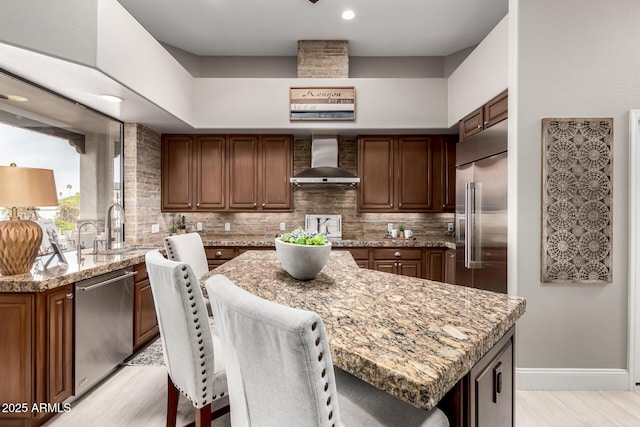 kitchen featuring a sink, stainless steel appliances, wall chimney exhaust hood, tasteful backsplash, and a center island