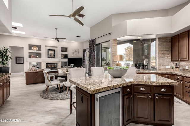 kitchen with visible vents, beverage cooler, a sink, a glass covered fireplace, and ceiling fan