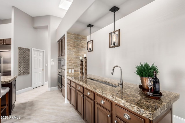 kitchen featuring a peninsula, stone countertops, a sink, decorative light fixtures, and stainless steel built in refrigerator