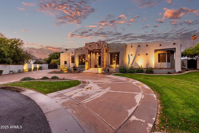 adobe home with a front lawn, stucco siding, fence, and curved driveway