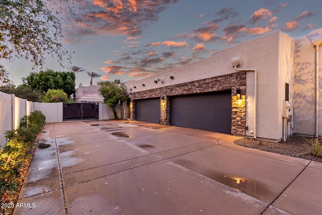 property exterior at dusk with stucco siding, an attached garage, driveway, and a gate