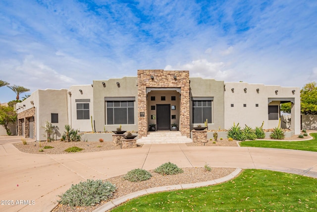 adobe home with stone siding, stucco siding, and curved driveway