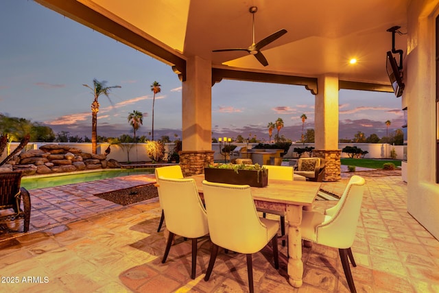 patio terrace at dusk with outdoor dining area, a fenced backyard, and a ceiling fan