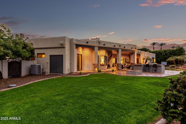 back of house at dusk featuring outdoor dry bar, a gate, a patio, a yard, and central AC unit