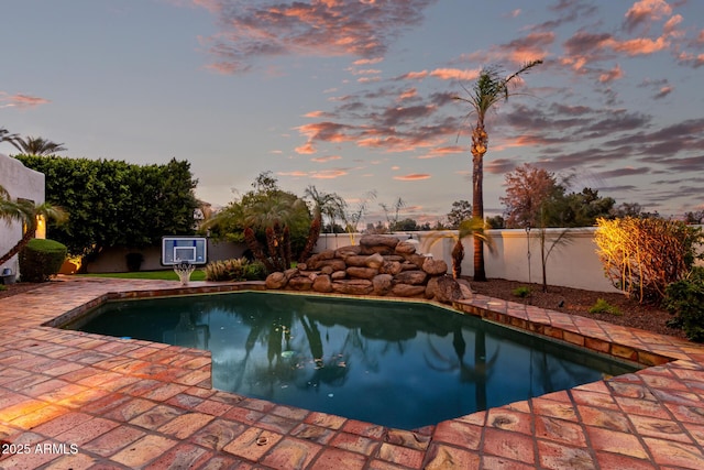 pool at dusk featuring a patio, a fenced backyard, and a fenced in pool