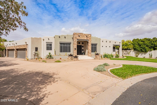 adobe home with stucco siding, stone siding, curved driveway, and fence