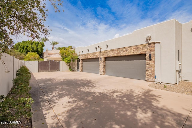 view of side of property featuring stucco siding, driveway, a gate, fence, and an attached garage